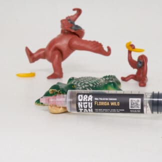 Orangutan Trading Co spore syringe with three toy orangutans and an alligator playing with it, white background