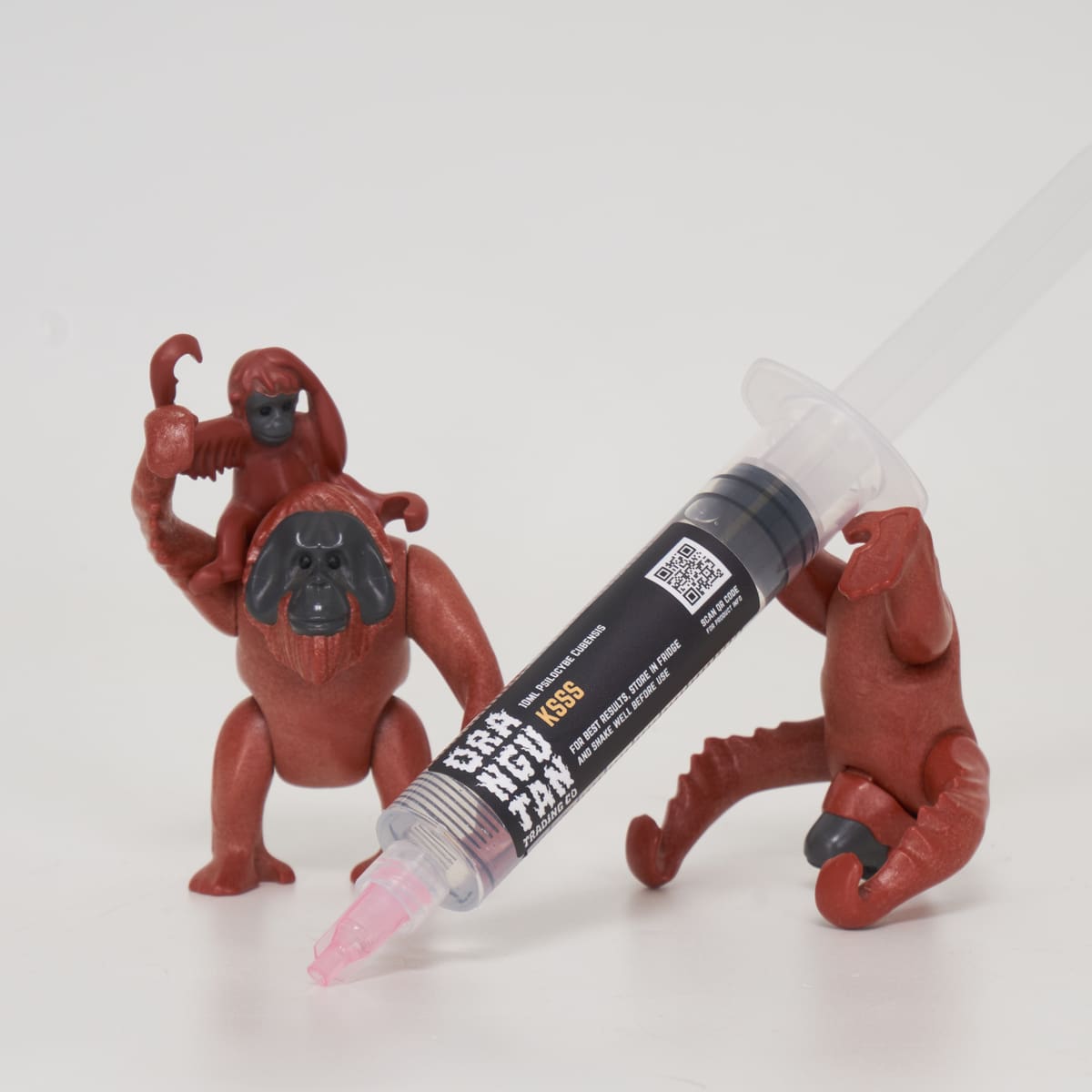 Orangutan Trading Co spore syringe with three toy orangutans playing with it, white background