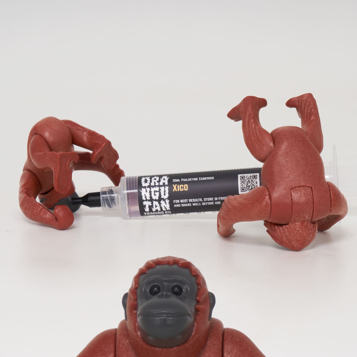 Orangutan Trading Co spore syringe with three toy orangutans playing with it, white background